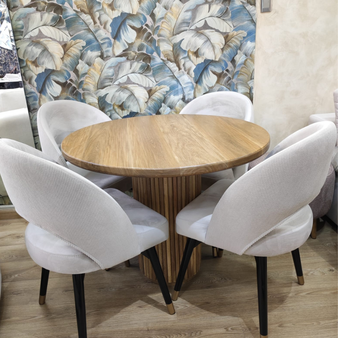 Comedor Toscana con mesa redonda en madera flor morado y sillas tapizadas beige.