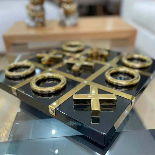 Tablero decorativo Tic Tac Toe dorado con base negra sobre mesa de centro elegante