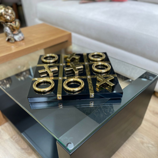Tablero decorativo Tic Tac Toe dorado con base negra sobre mesa de centro elegante